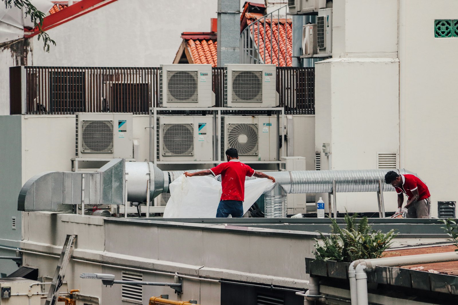 Two PrimeFix technicians installing condensing units on a commercial rooftop.