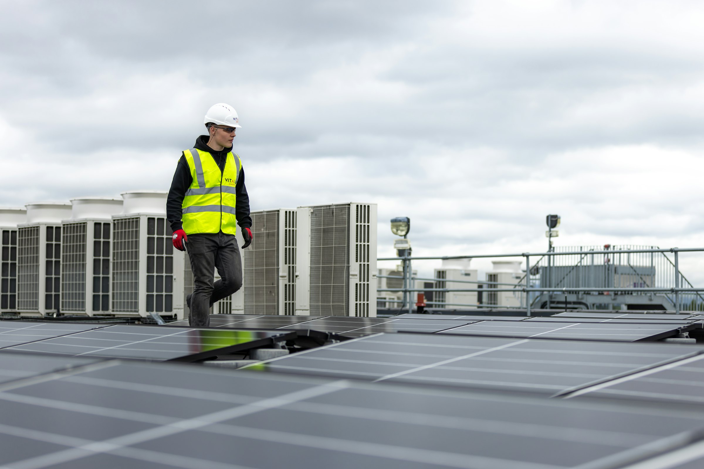 A PrimeFix technician walking a commercial rooftop lined with condensing units.